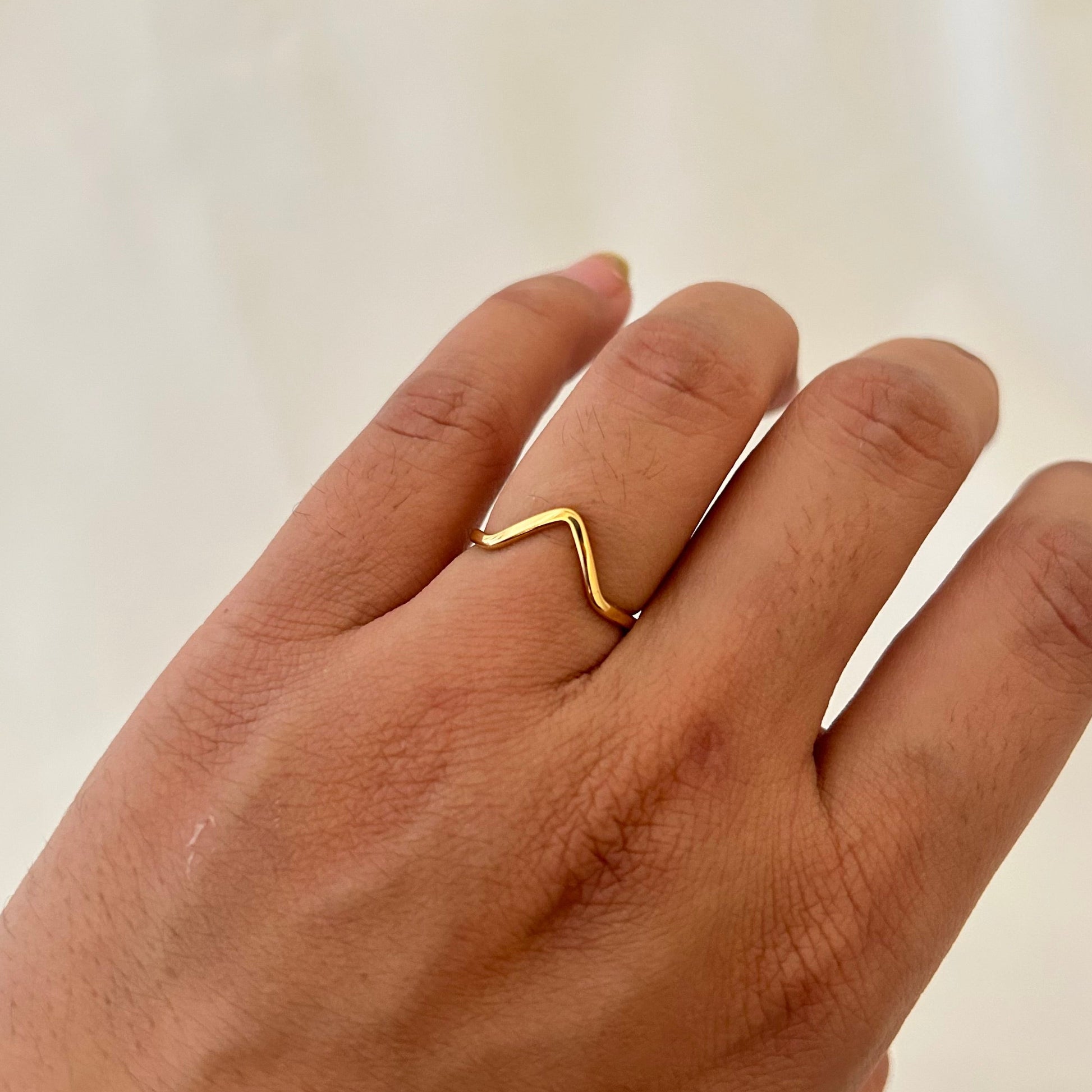 Hand wearing a thin gold ring shaped in a soft wave pattern.