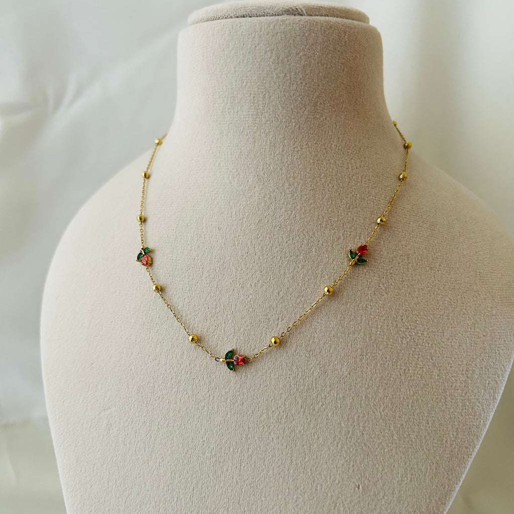 Minimal gold necklace with tiny red and green floral charms displayed on a mannequin bust.