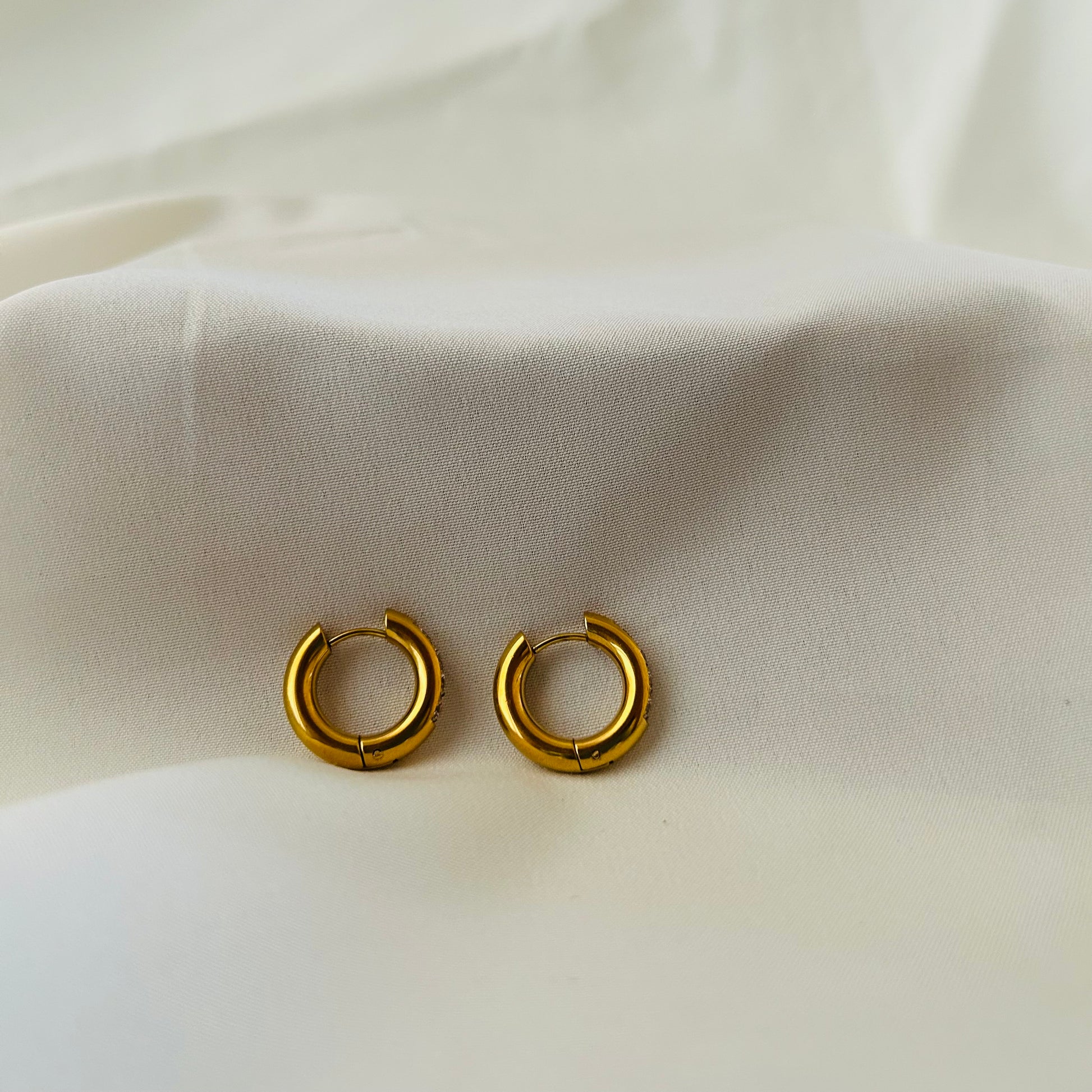 Gold hoop earrings with embedded crystal stones hanging on a wooden display rod.