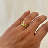 Hand wearing a gold abstract snake-shaped ring with an open, flowing design.