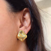Gold irregular nugget shaped stud earrings on pink background.