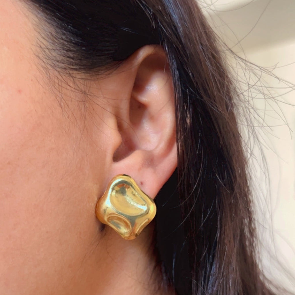 Gold irregular nugget shaped stud earrings on pink background.