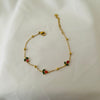 Delicate gold bracelet with small red and green floral charms placed on white fabric.