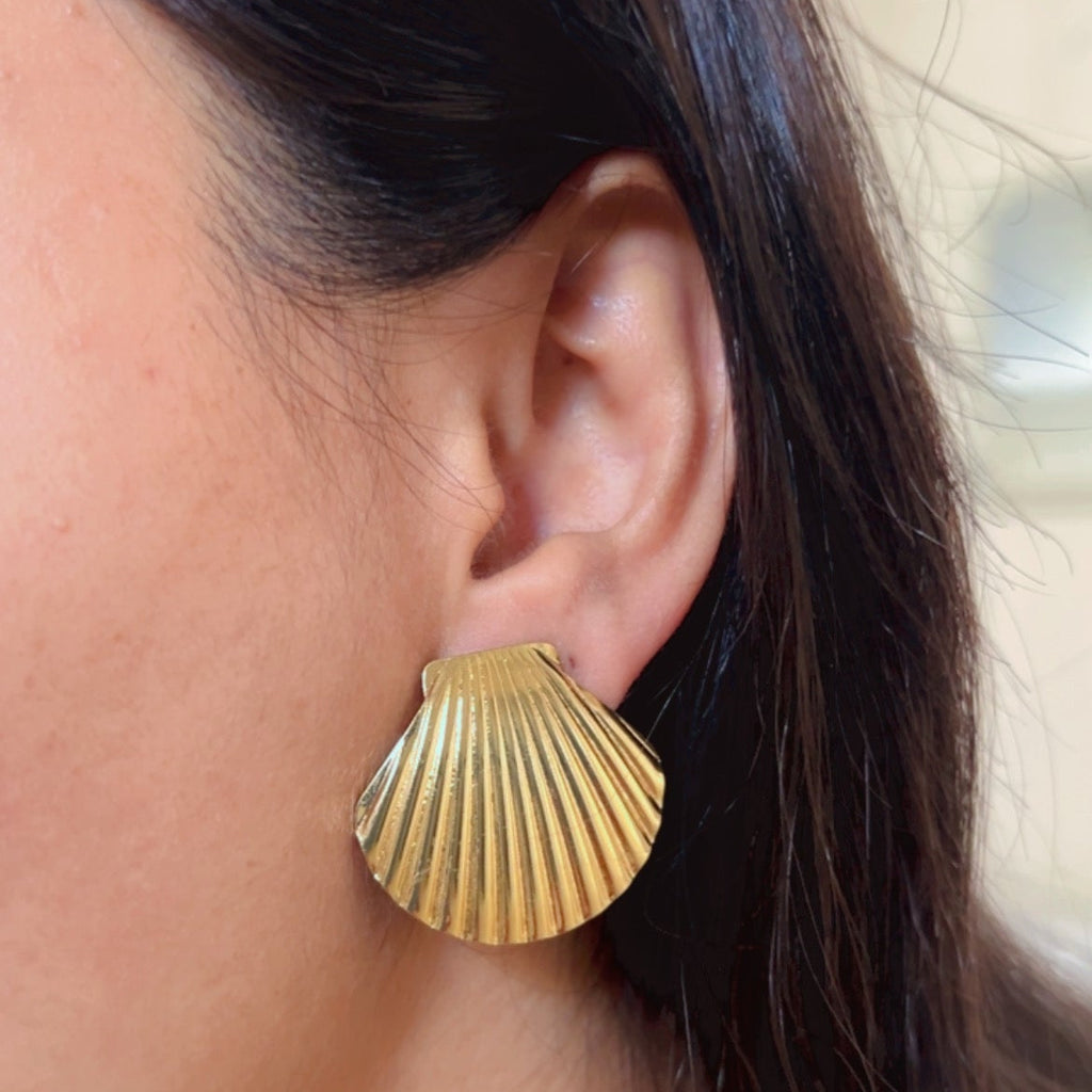 Gold shell textured stud earrings on pink background.