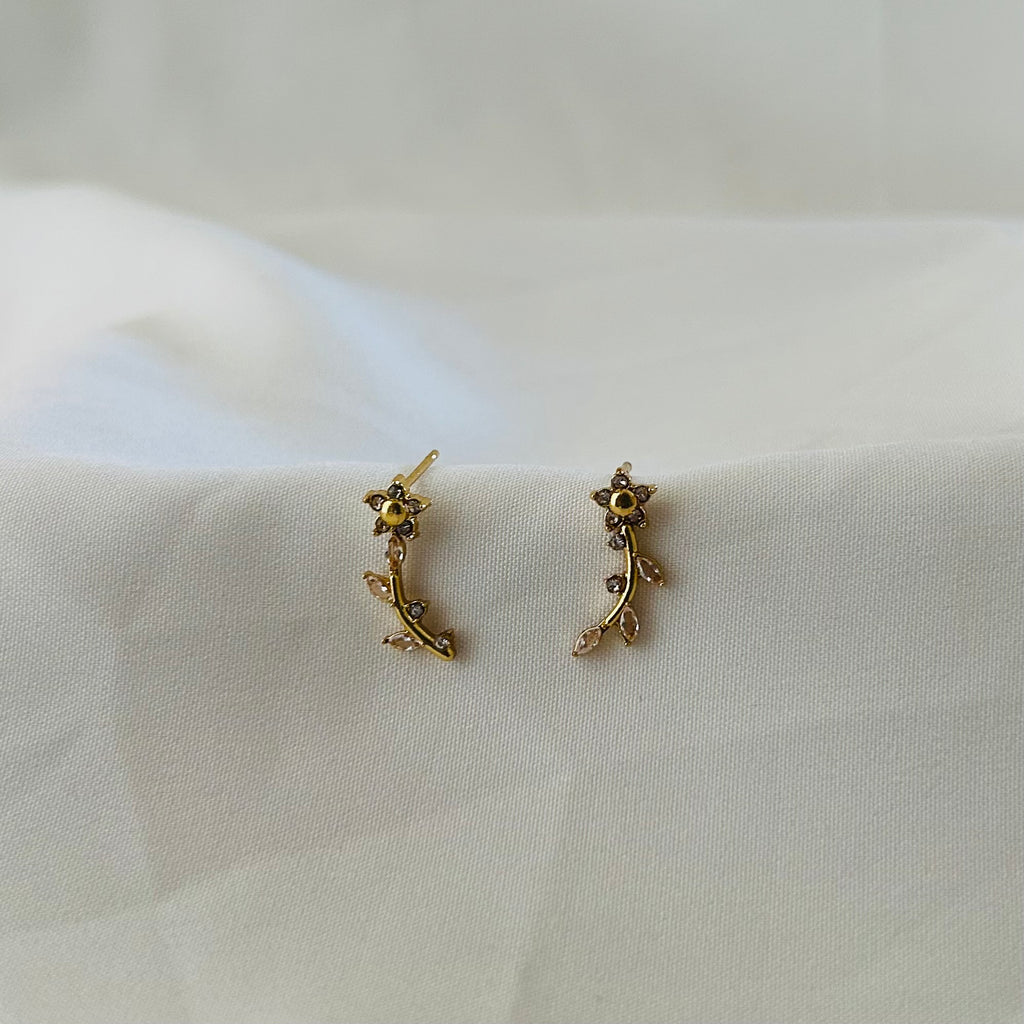Gold floral vine-style ear climber earrings with crystal accents placed on white fabric.