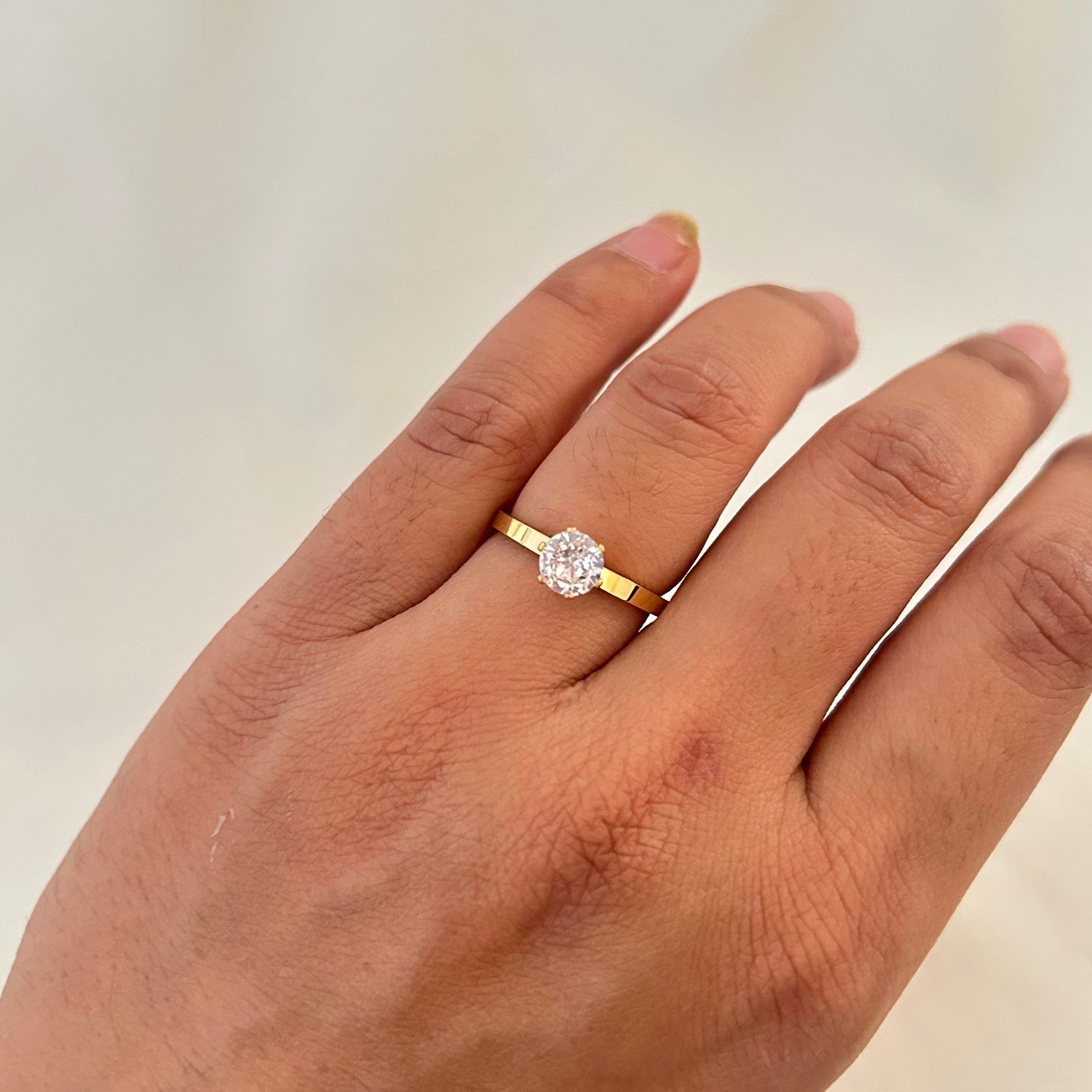 Hand wearing a gold ring with a single oval-cut clear gemstone on a thin polished band.