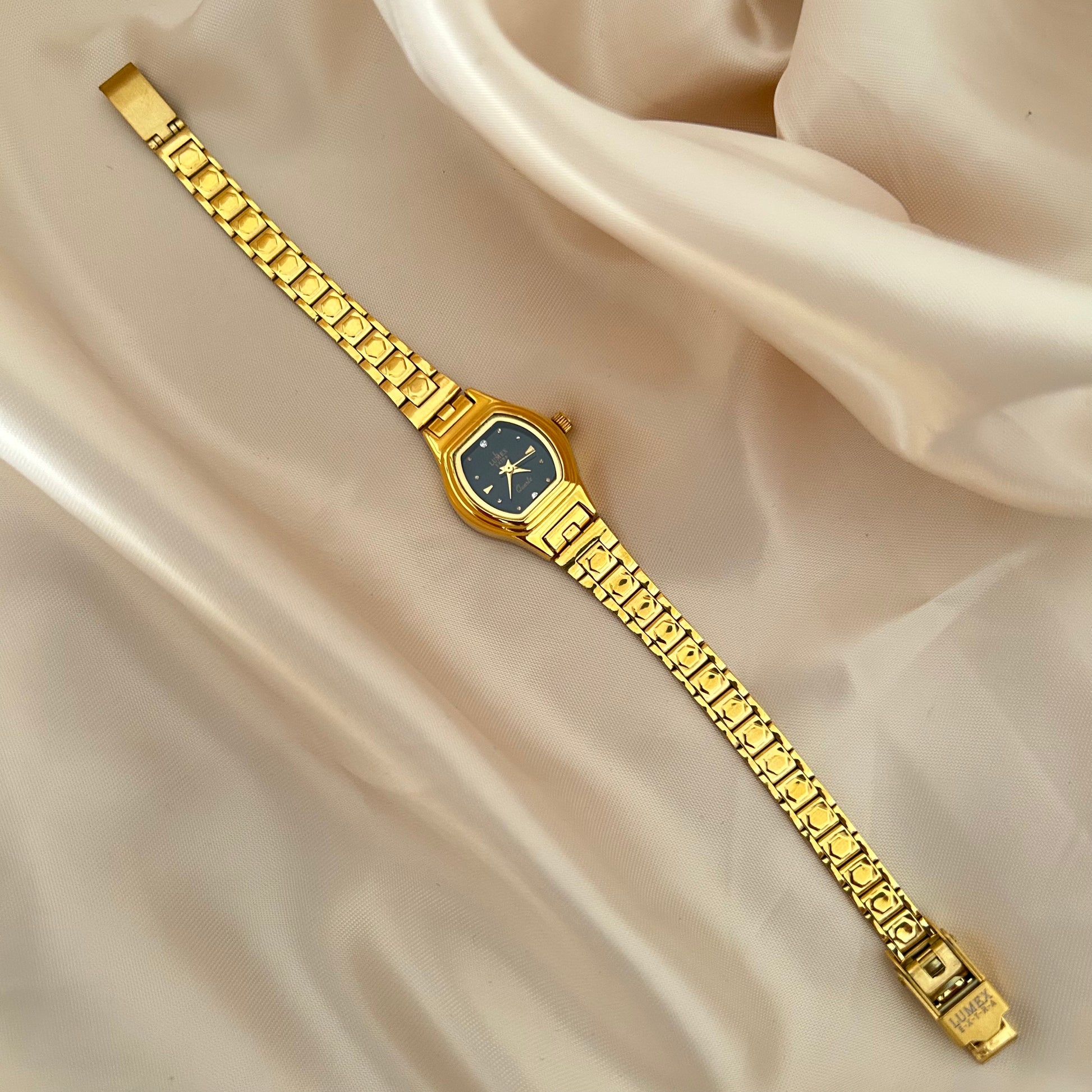 Gold Circle dial wristwatch with linked bracelet placed on soft beige satin background, elegant minimal design.