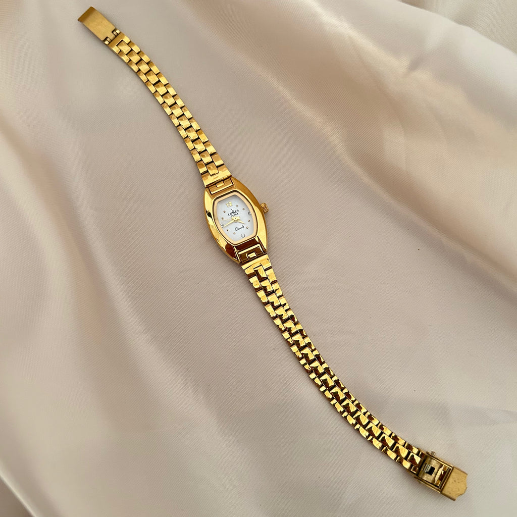 Gold oval dial wristwatch with linked bracelet placed on soft beige satin background, elegant minimal design.
