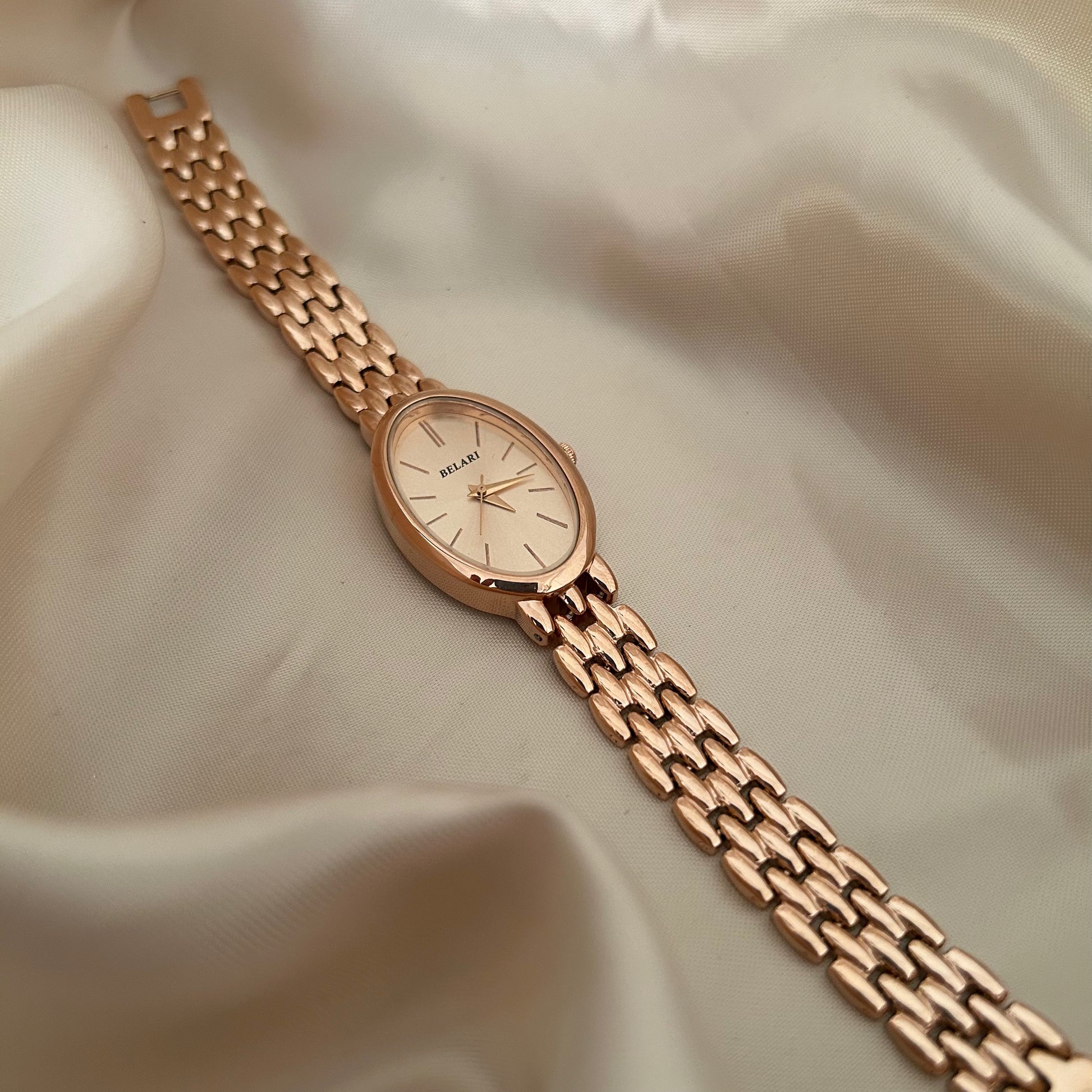 Rose gold wristwatch with Rose gold dial and metal strap on soft satin background.