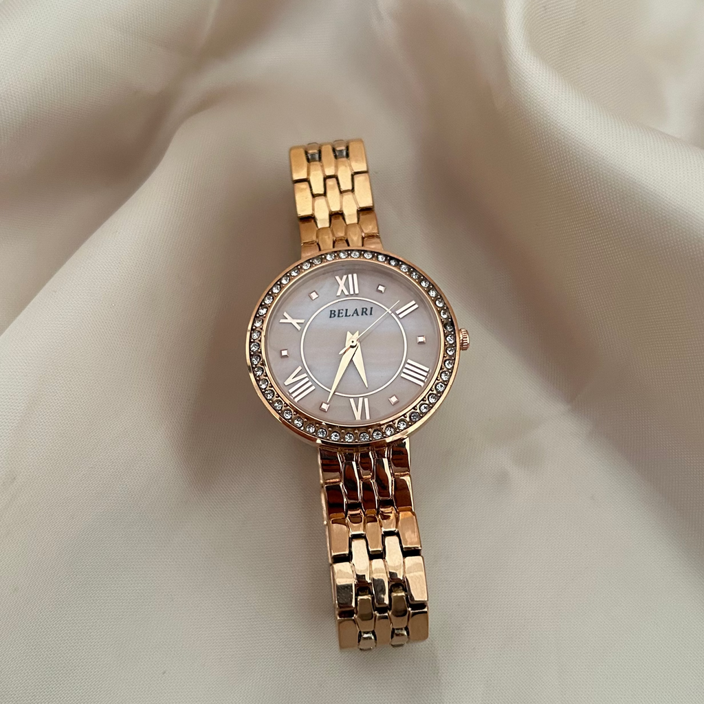 Rose gold wristwatch with Roman numeral dial and crystal studded bezel on soft satin background.