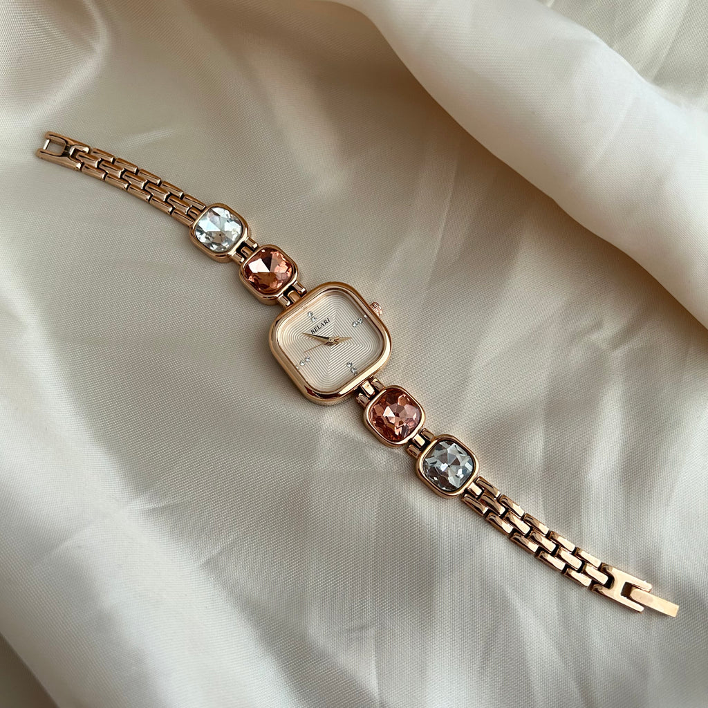 Gold wristwatch with gemstone bracelet links and square dial on satin background.