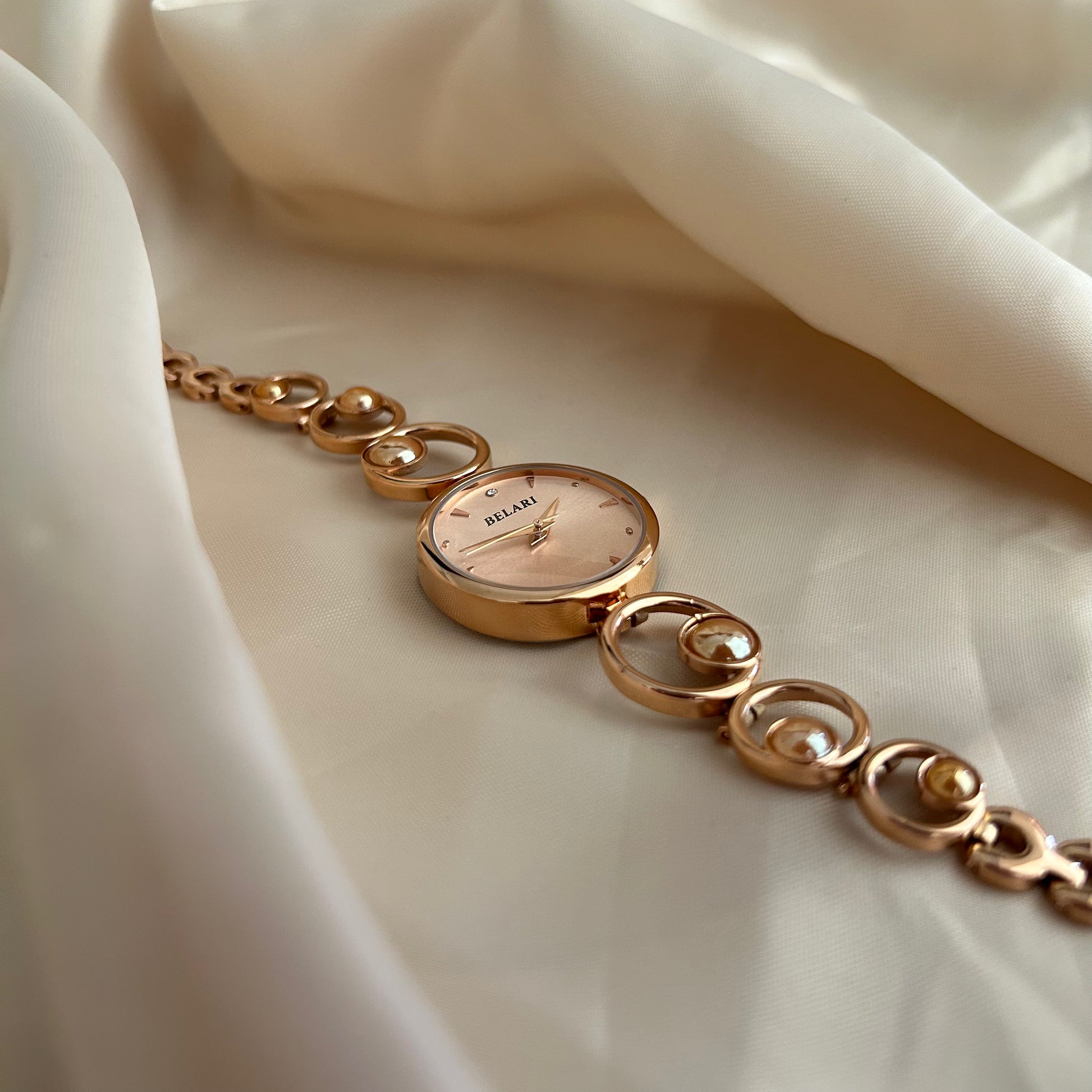Rose gold wristwatch with pearl bracelet design and round dial on soft satin background.