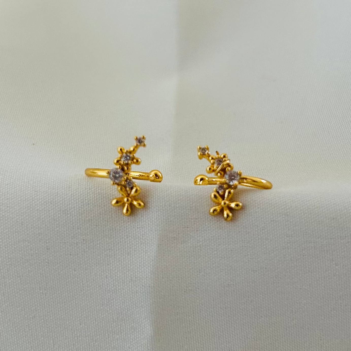 Gold floral ear cuff with small crystal accents in a delicate design, minimal and stylish jewelry piece placed on a soft neutral background for elegant wear.